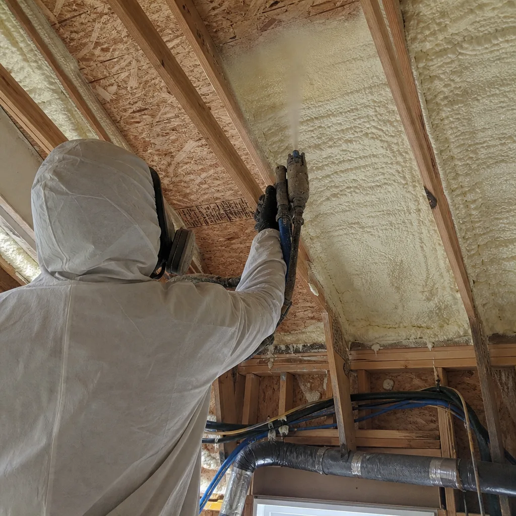 Contractor applying professional spray foam insulation to a residential attic ceiling.